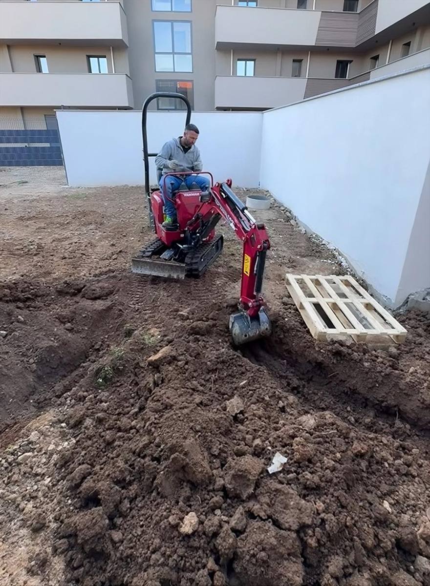 Miniescavatore che movimenta la terra nel cortile di un condominio, fra il muro di confine e il pozzetto già posato